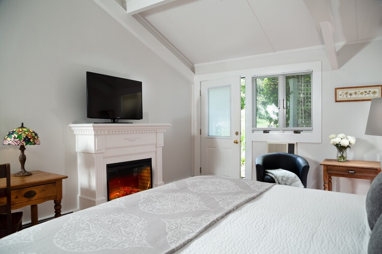 Gray room with white fireplace, lit and television on top of the mantle. Big bed is in the front part of the picture