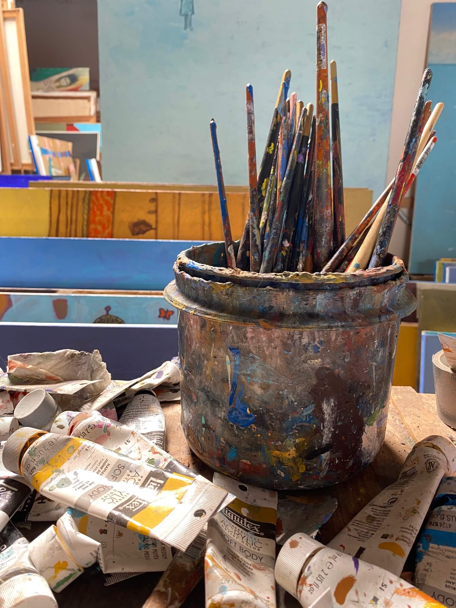 tubes of squished paint and a cup filled with many used, c colorful paintbrushes